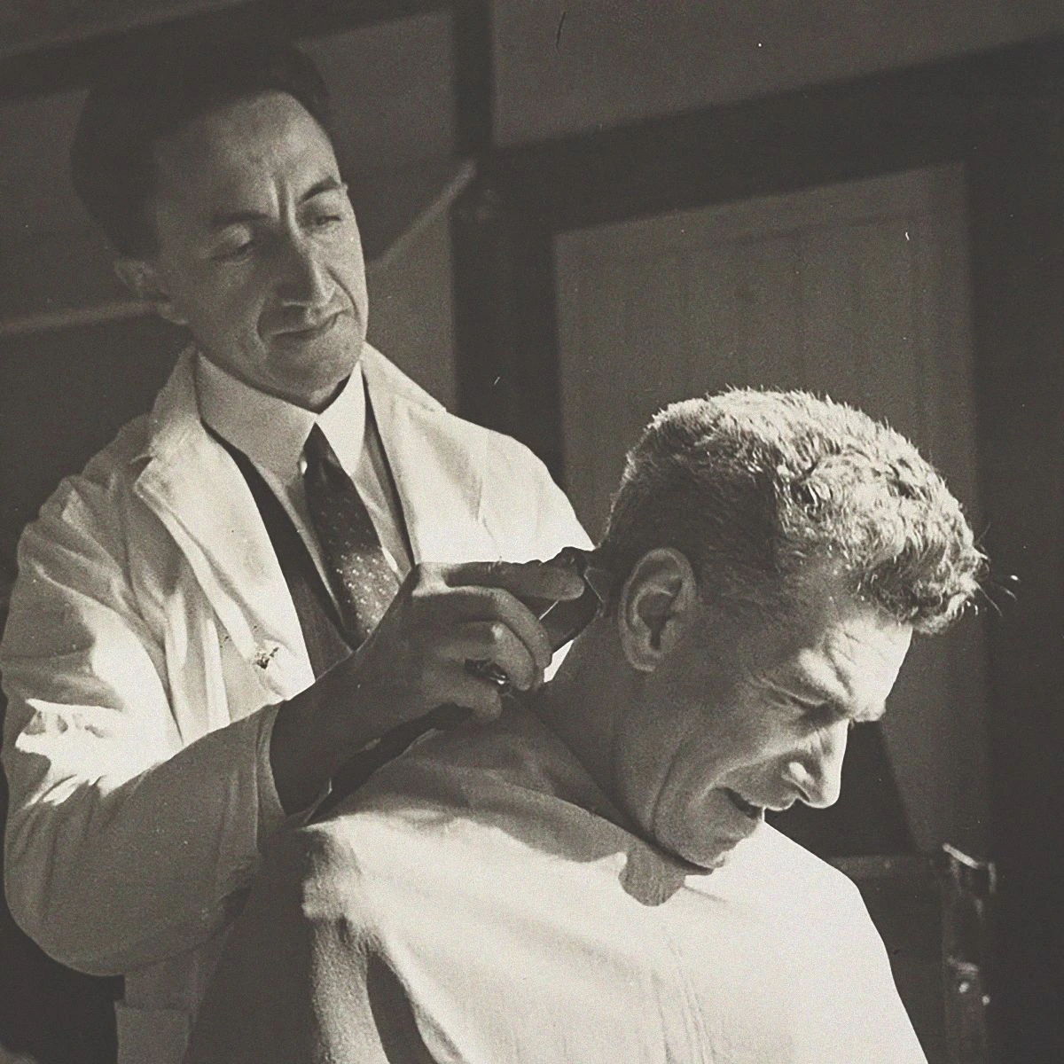 A barber cutting a man's hair in a vintage barbershop setting.