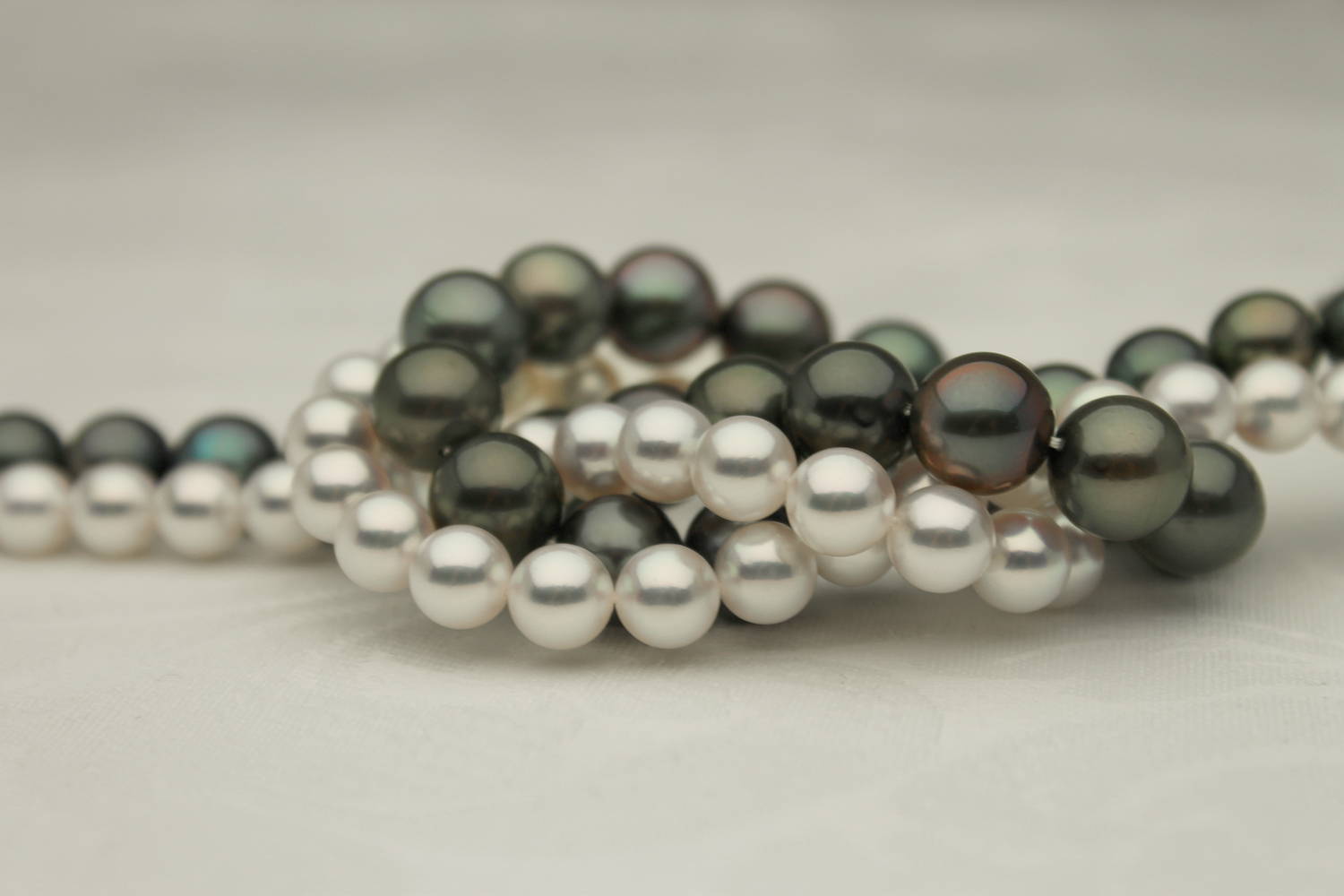 Black Tahitian Pearls and White Akoya Pearls Twisted Together In Front of a Grey Background