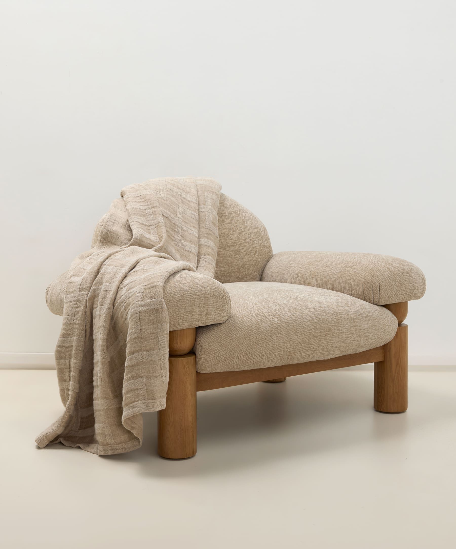 Beige armchair with a blanket draped over it on a white background