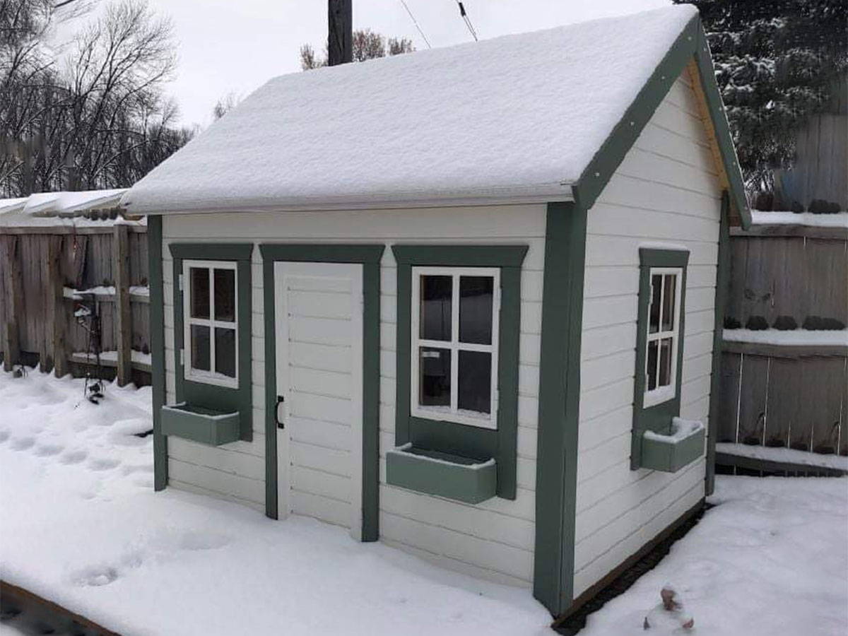  White and green Wooden Playhouse Natural Wonder covered with snow in a backyard by WholeWoodPlayhouses