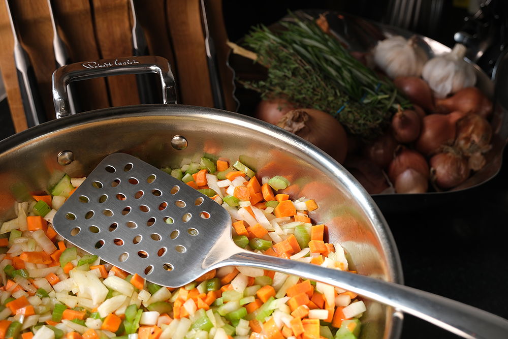 Sautéed vegetables in a 316 Series Low Casserole with a slotted spatula and garlic in background.