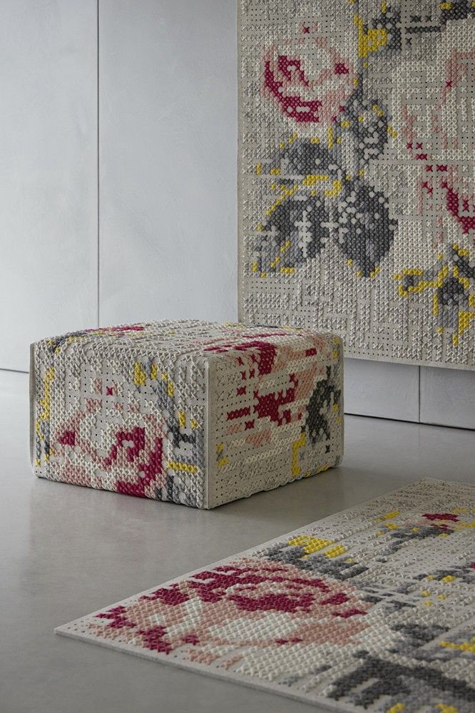A textured ottoman beside a colorful floral rug against a modern wall.