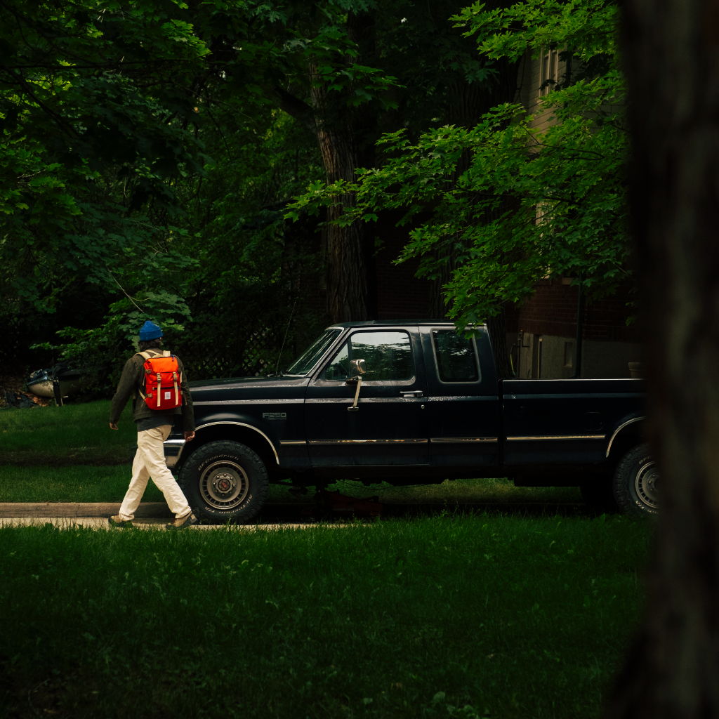 Person walking near a black pickup truck in a wooded area.