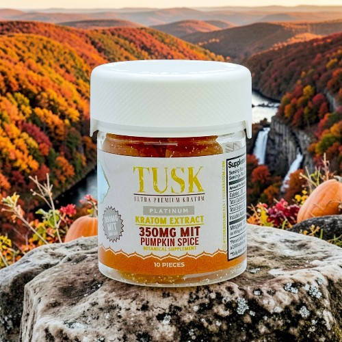 Bottle of Tusk pumpkin spice supplement against a colorful autumn landscape.