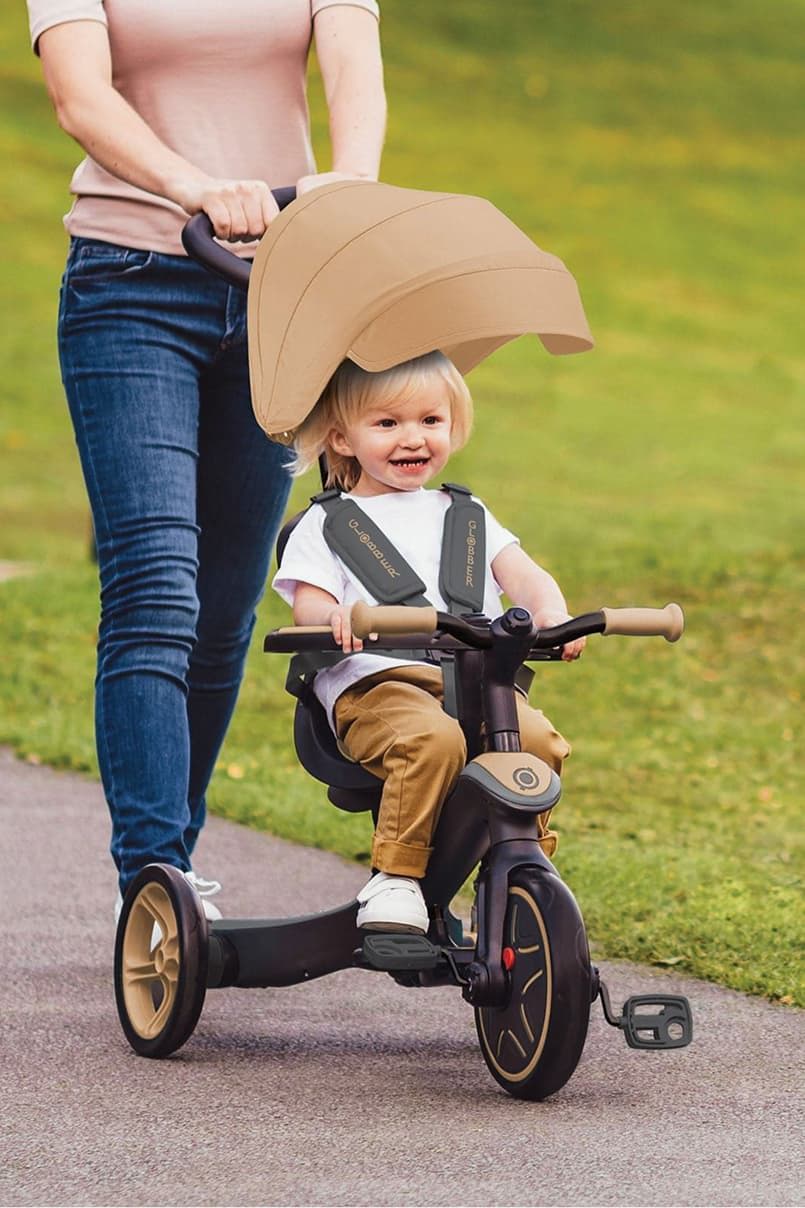 Child riding a tricycle with a parent walking beside on a path.