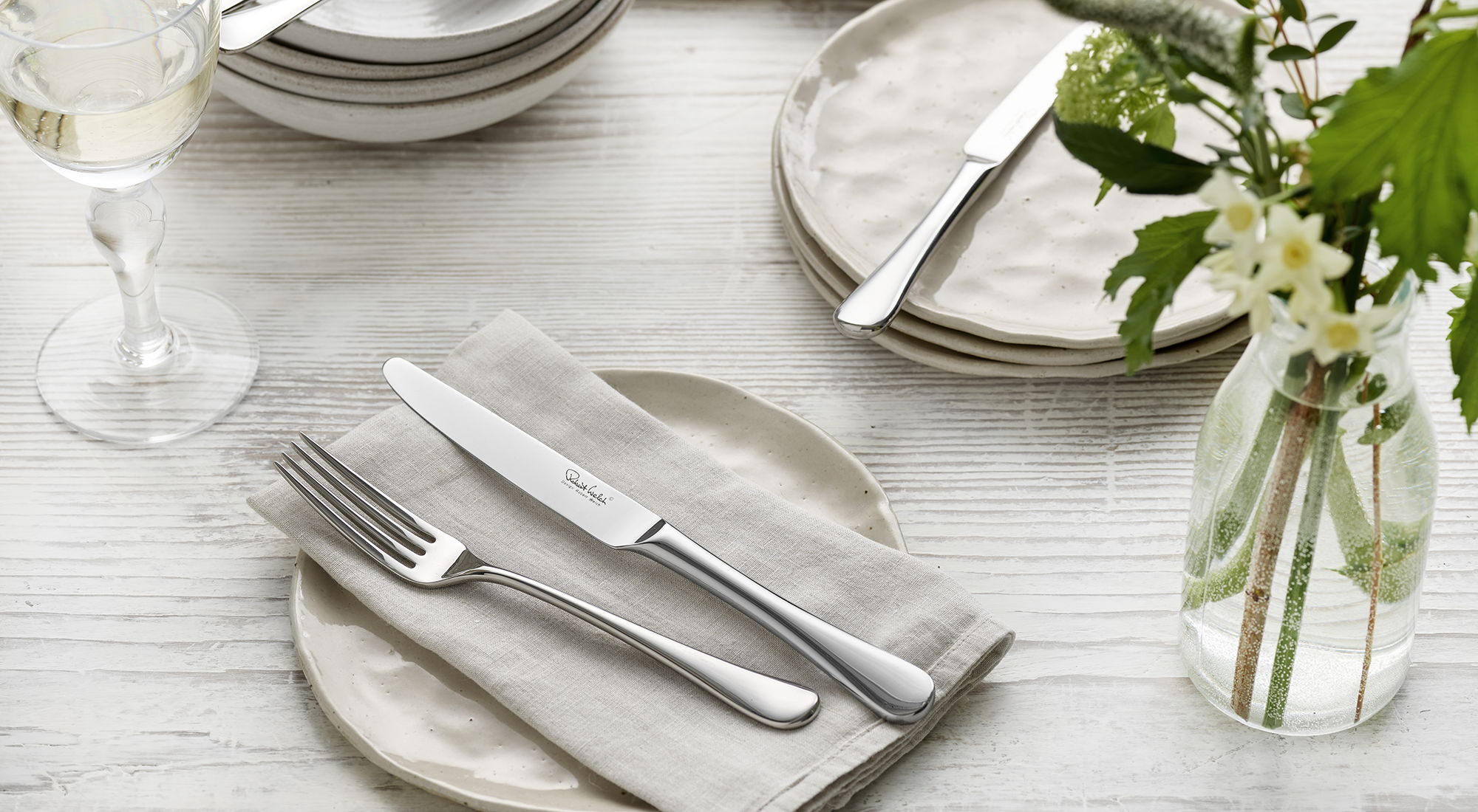 Set dining table with plates, Radford Bright cutlery, and a vase of flowers.