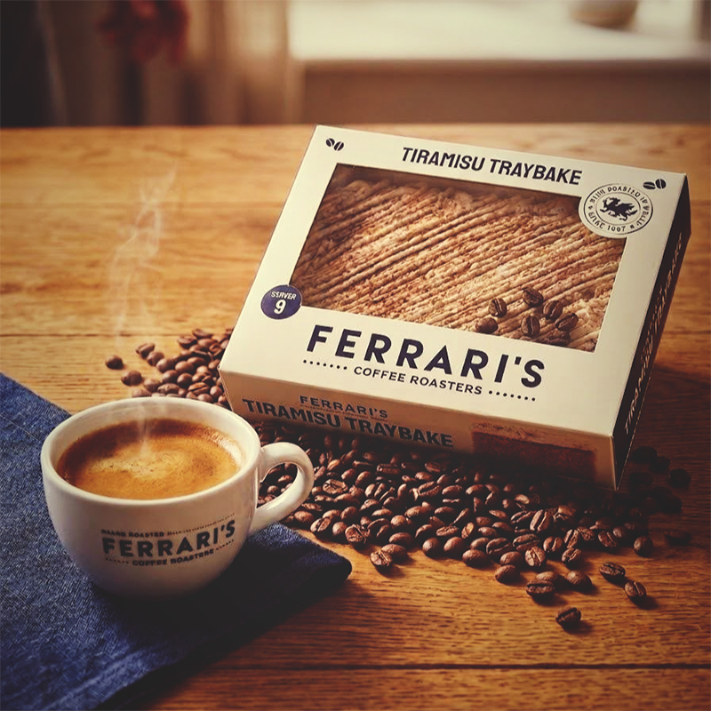 Ferraris Coffee Tiramisu Traybake made by Just Love Food Company, displayed with a cup of espresso and roasted coffee beans on a rustic wooden table.