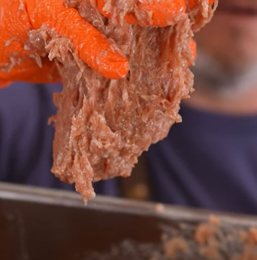 Person holding shredded meat with orange gloves, blurred background.