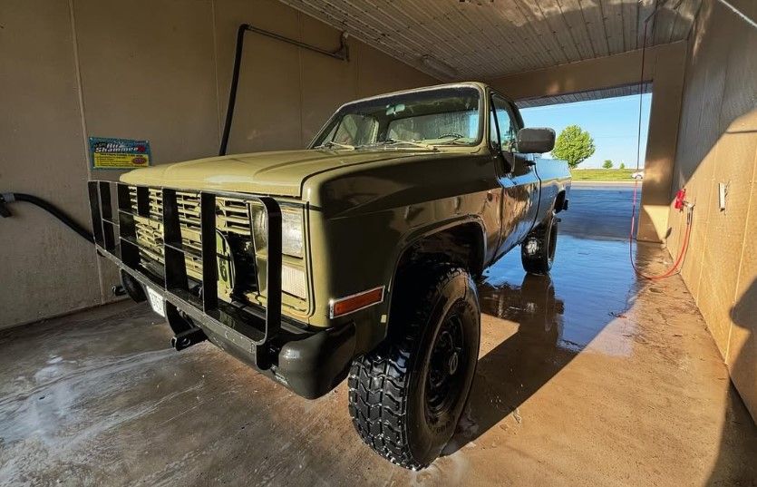 Front-three-quarter view Jacob's 1986 olive green Chevrolet K30 pickup in a car wash bay with black brush guard rectangular headlights and off-road tires on black rims HornBlasters Conductor's Special 127H train horn kit featured customer install gallery photo 1