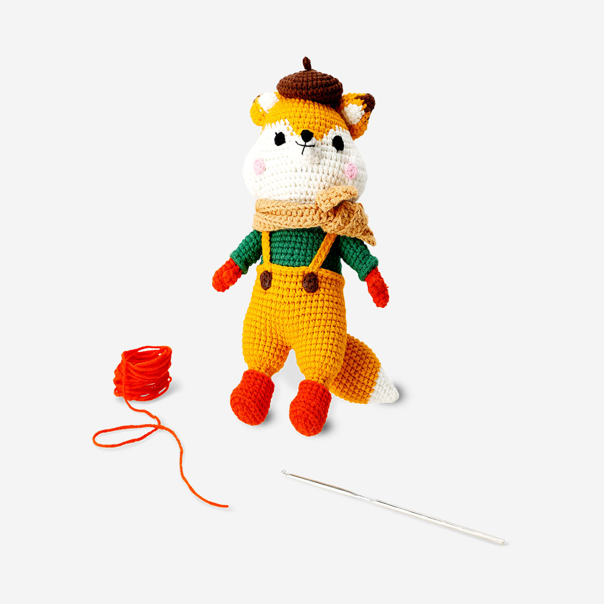 Hæklet rævedukke iført overalls og tørklæde, med garn og en nål.