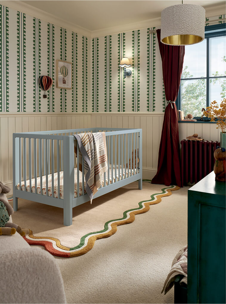 A cozy nursery with a cotbed, patterned wallpaper, and colorful rug.