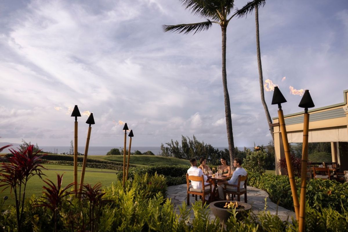 Group of people dining outdoors with palm trees and tiki torches.