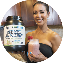Photo of India Paulino posing with a container of Vegan Protein powder in hand and a strawberry shake