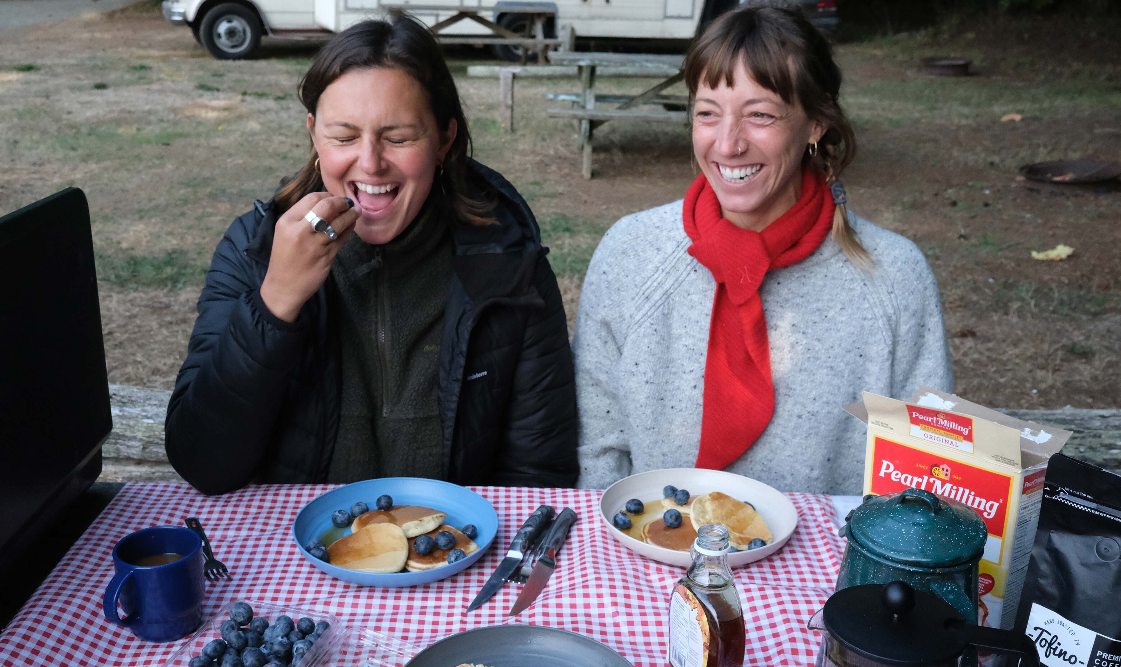 Two women enjoying breakfast outdoors, smiling, with plates of food in front.