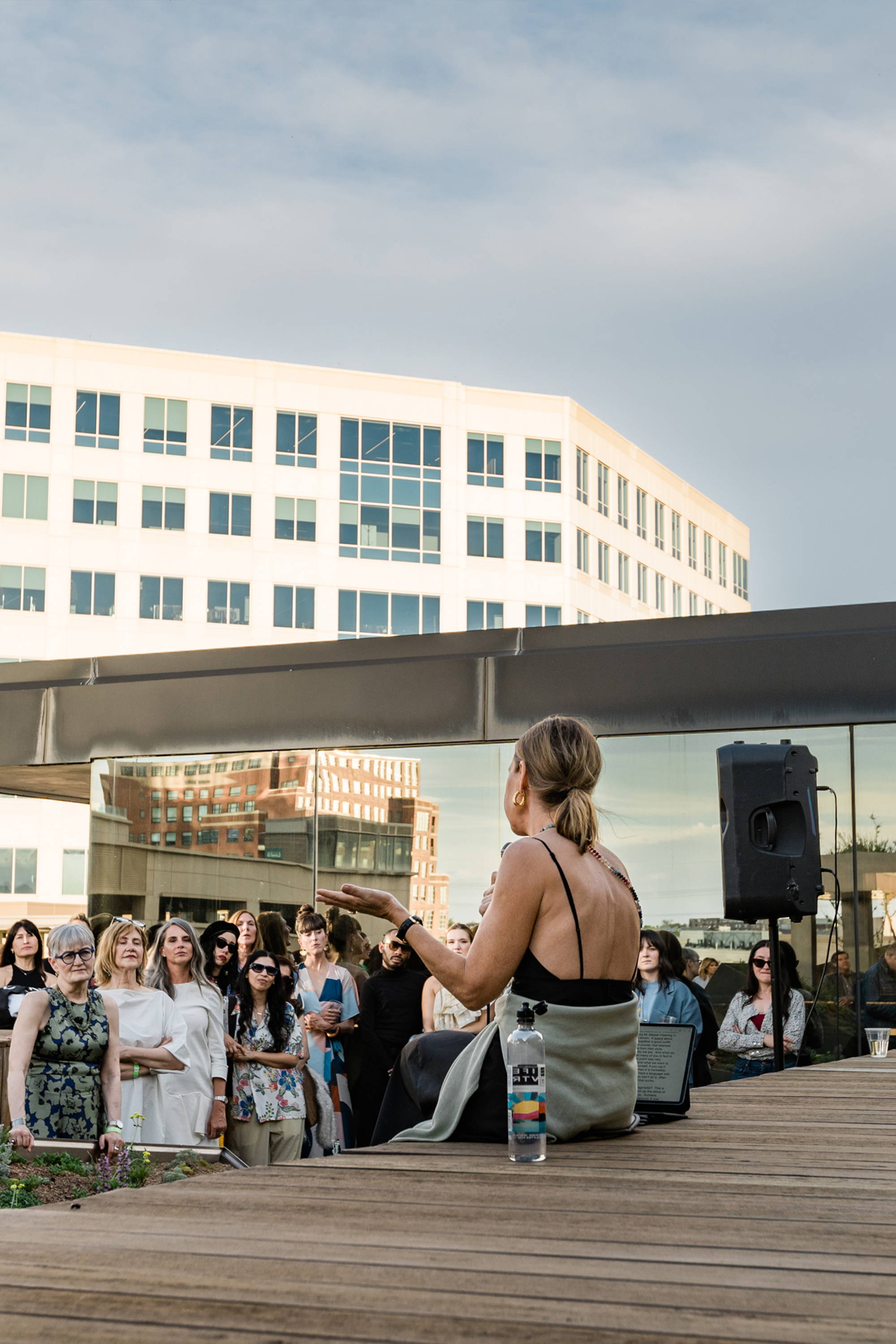 Person speaking to an audience outdoors near a building.