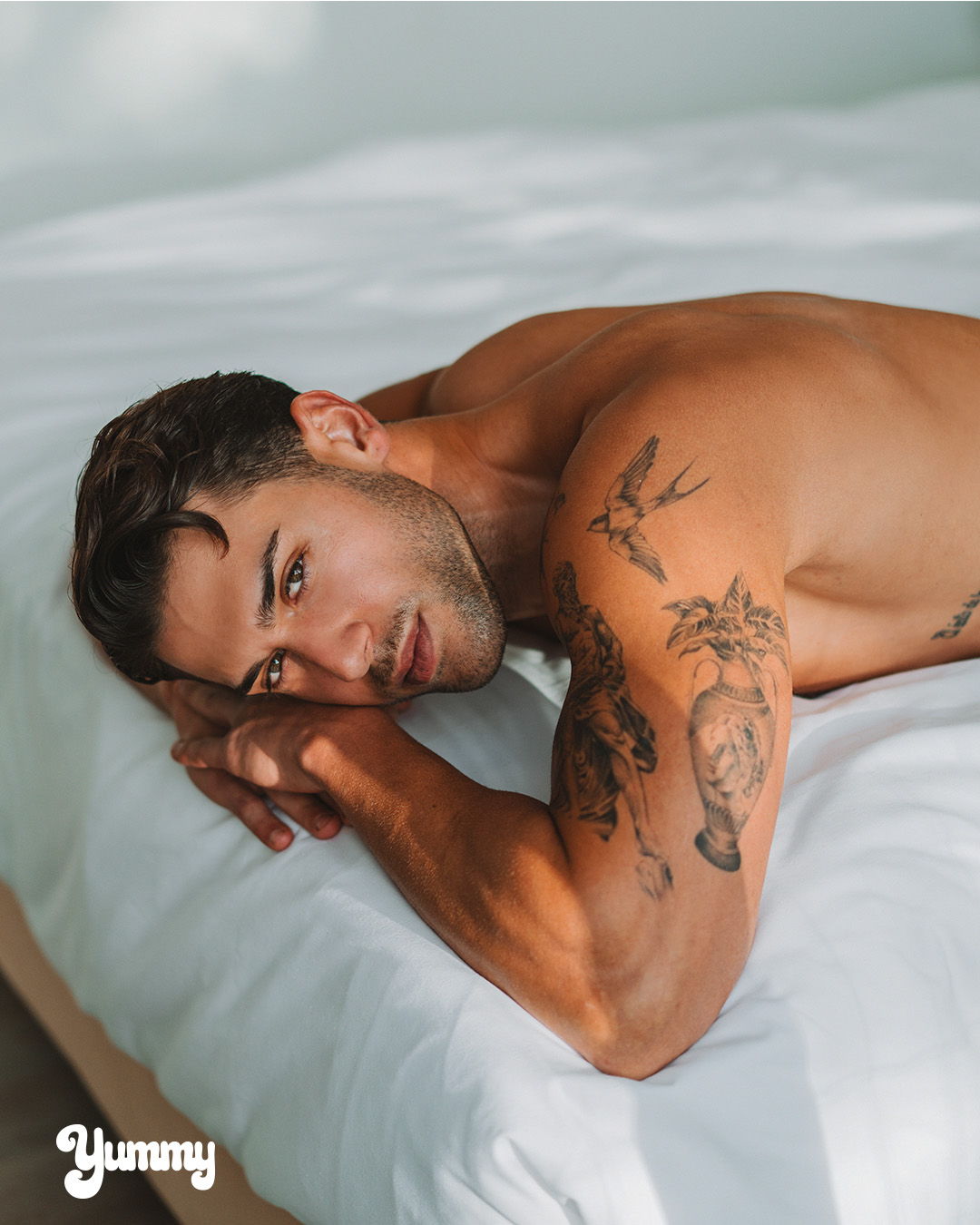A shirtless man with tattoos lying on a bed.