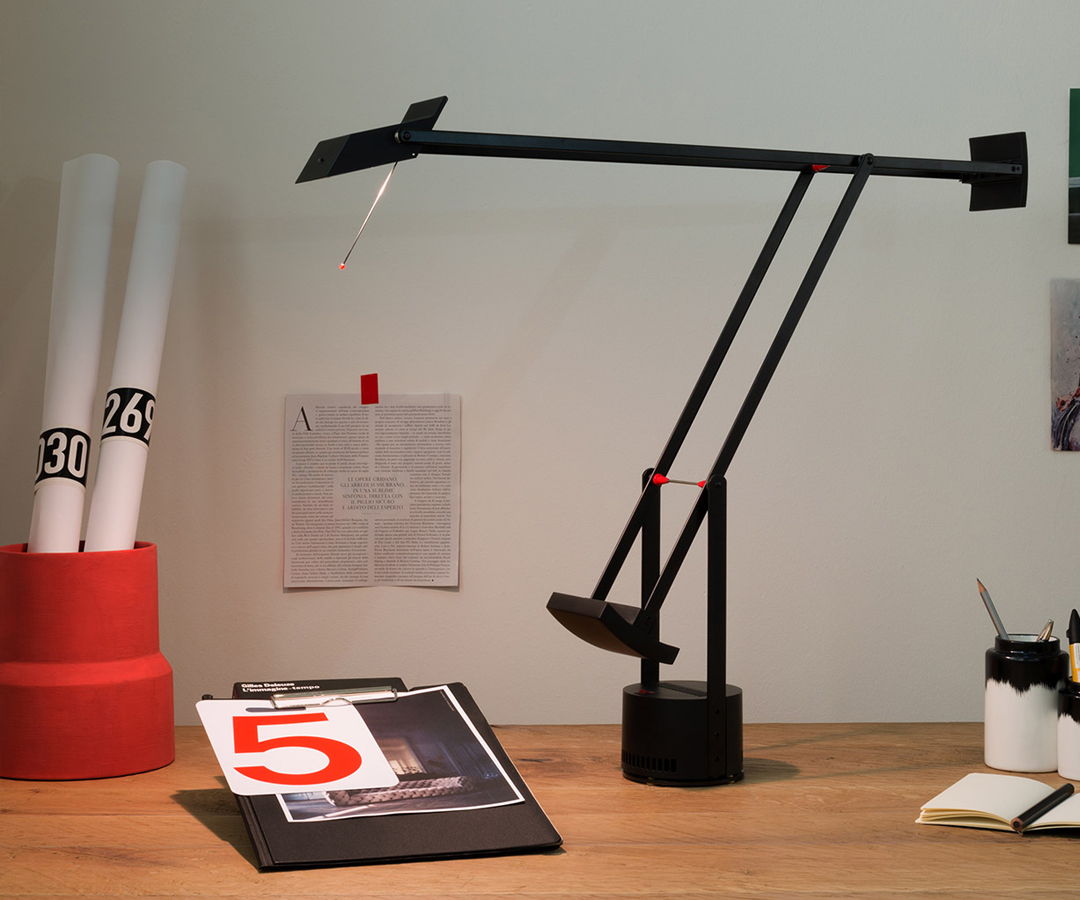 Desk with a Tizio lamp by Artemide, papers, and a red container.