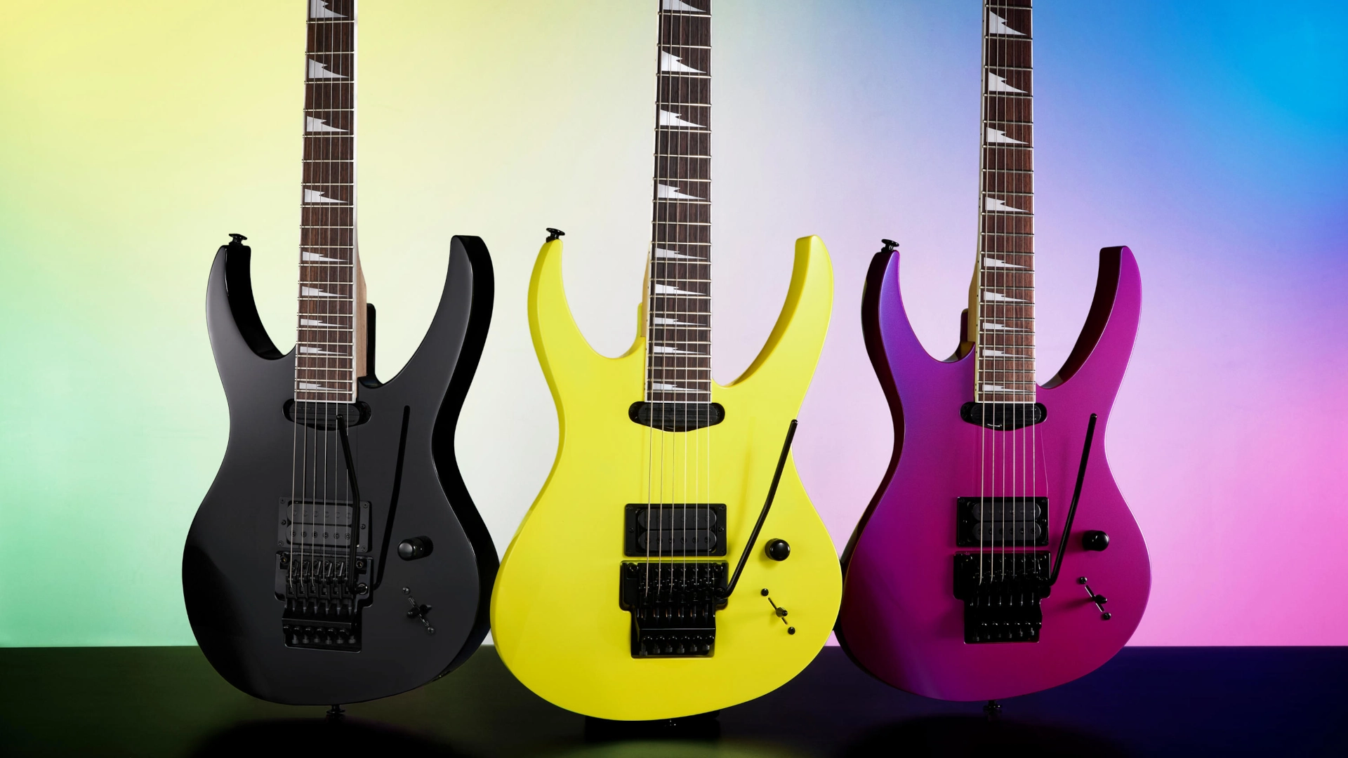 Three Ibanez P Series 540PIII electric guitars in black, yellow, and purple against a colorful background.