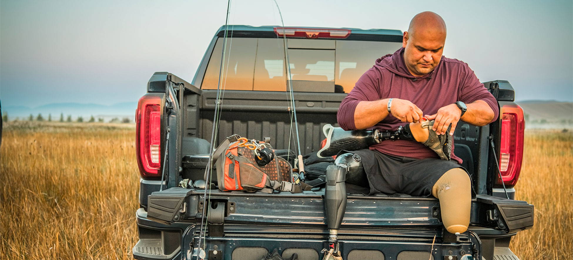 Man with prosthetic legs on tailgate of pickup truck.