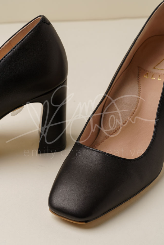 Black high-heeled shoes with a square toe on a neutral background.