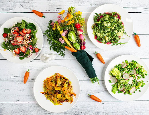 Assorted colorful salads and a bouquet of fresh vegetables on a wooden table.