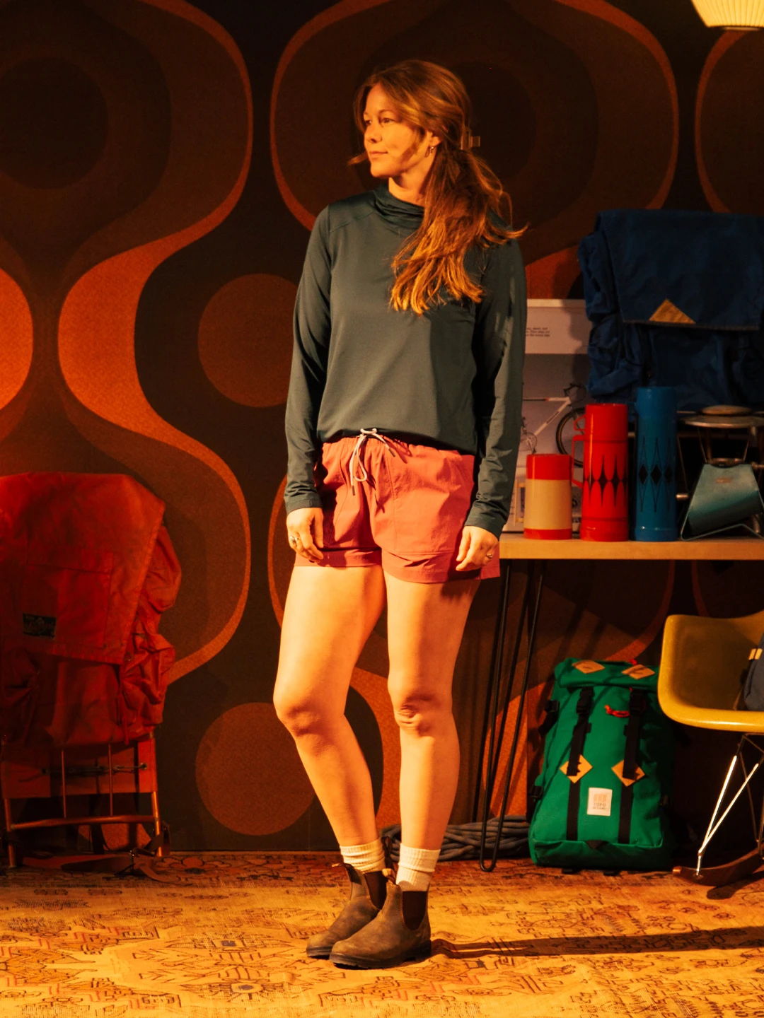 A woman in casual attire stands in a retro-themed room.