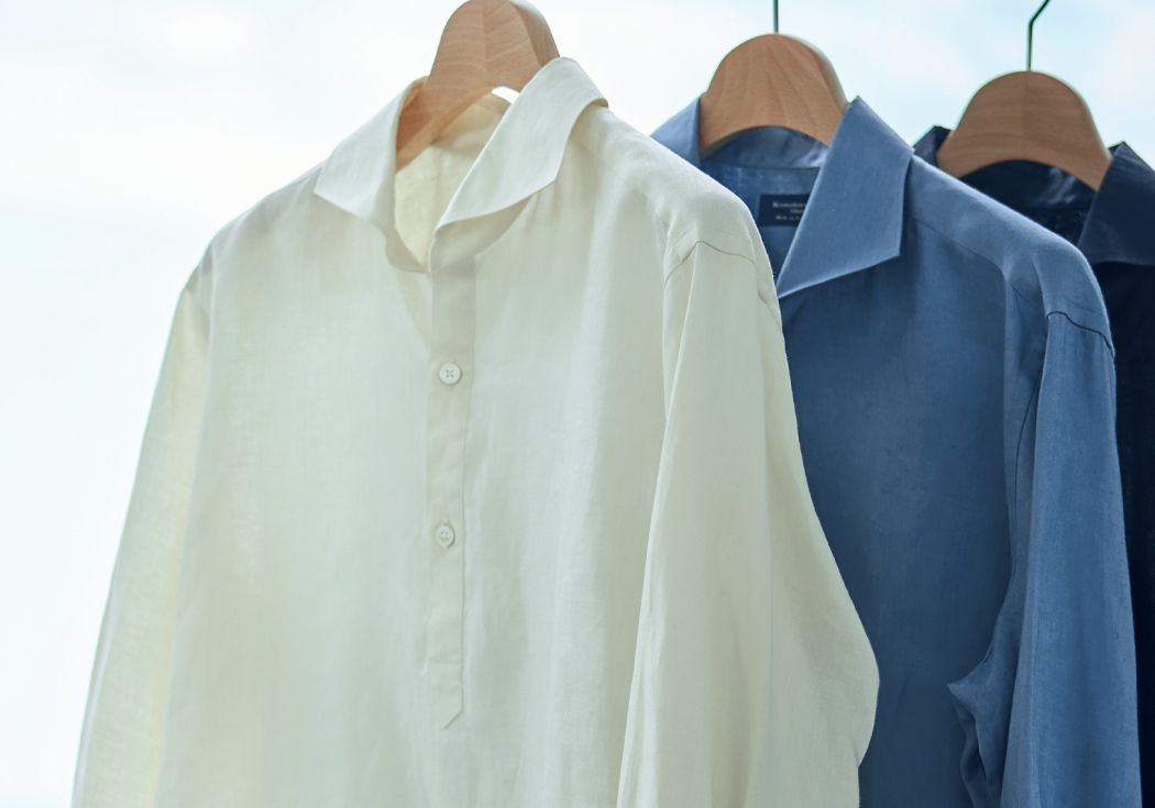 Three shirts hanging on wooden hangers against a bright background.