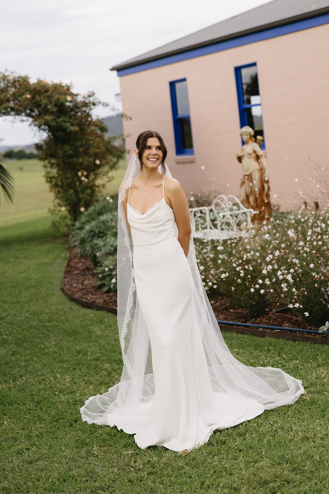 Bride in a white dress and veil standing in a garden.