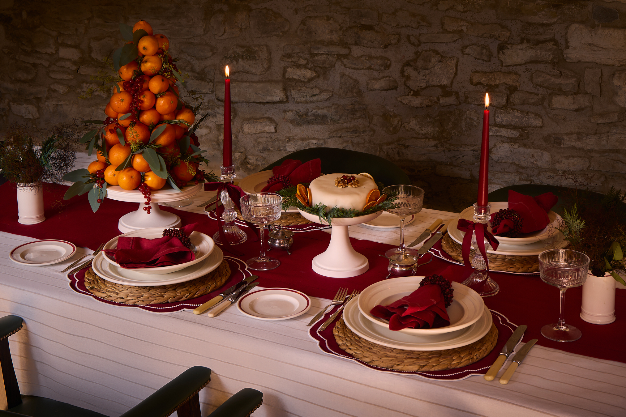 Table laid with white tablecloth, red runner and white ceramics including a porcelain display stand holding a christmas cake. 