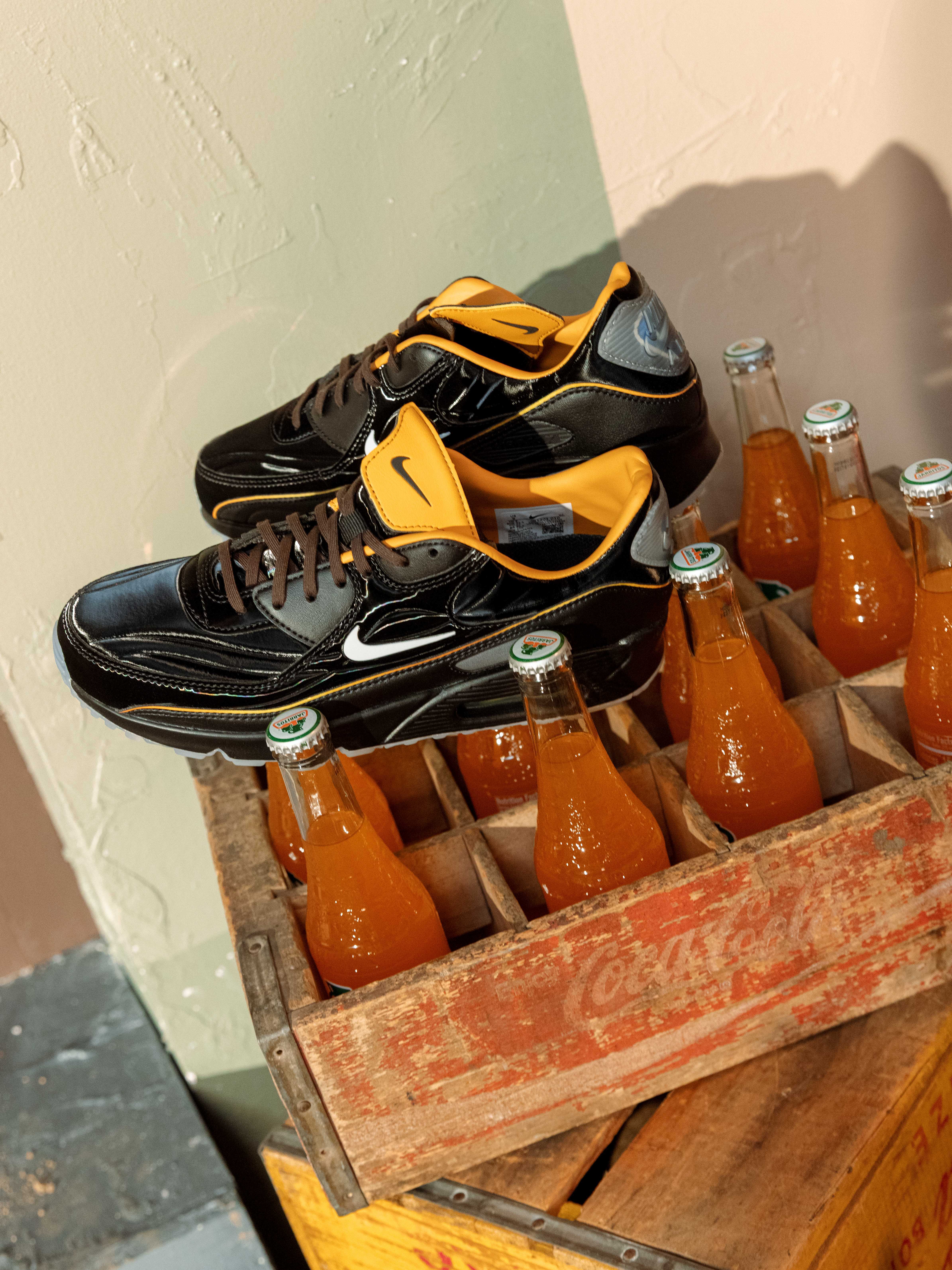 Black and orange Nike shoes on a wooden crate of orange soda bottles.