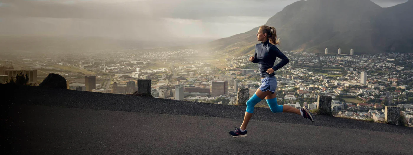 A woman runs along a scenic overlook with a city backdrop.