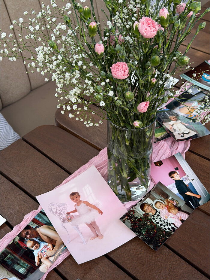 A vase of pink flowers surrounded by photographs on a table.