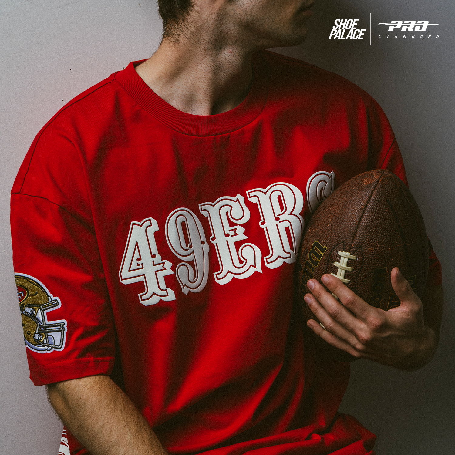 Person in a red shirt holding a football, partially turned away from the camera.