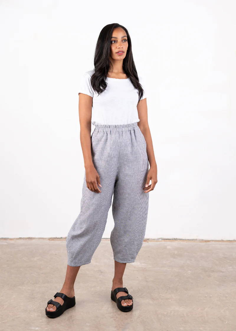 A model wearing a white tshirt with black and white striped linen barrel leg trousers and black chunky slides