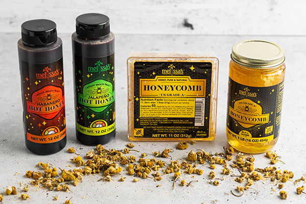 Bottles of honey and honeycomb on a table with scattered pollen.