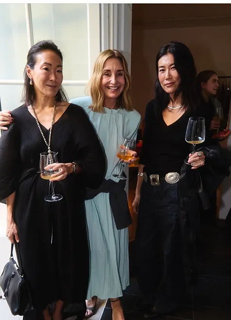 Three women posing together, holding drinks, in a stylish indoor setting.