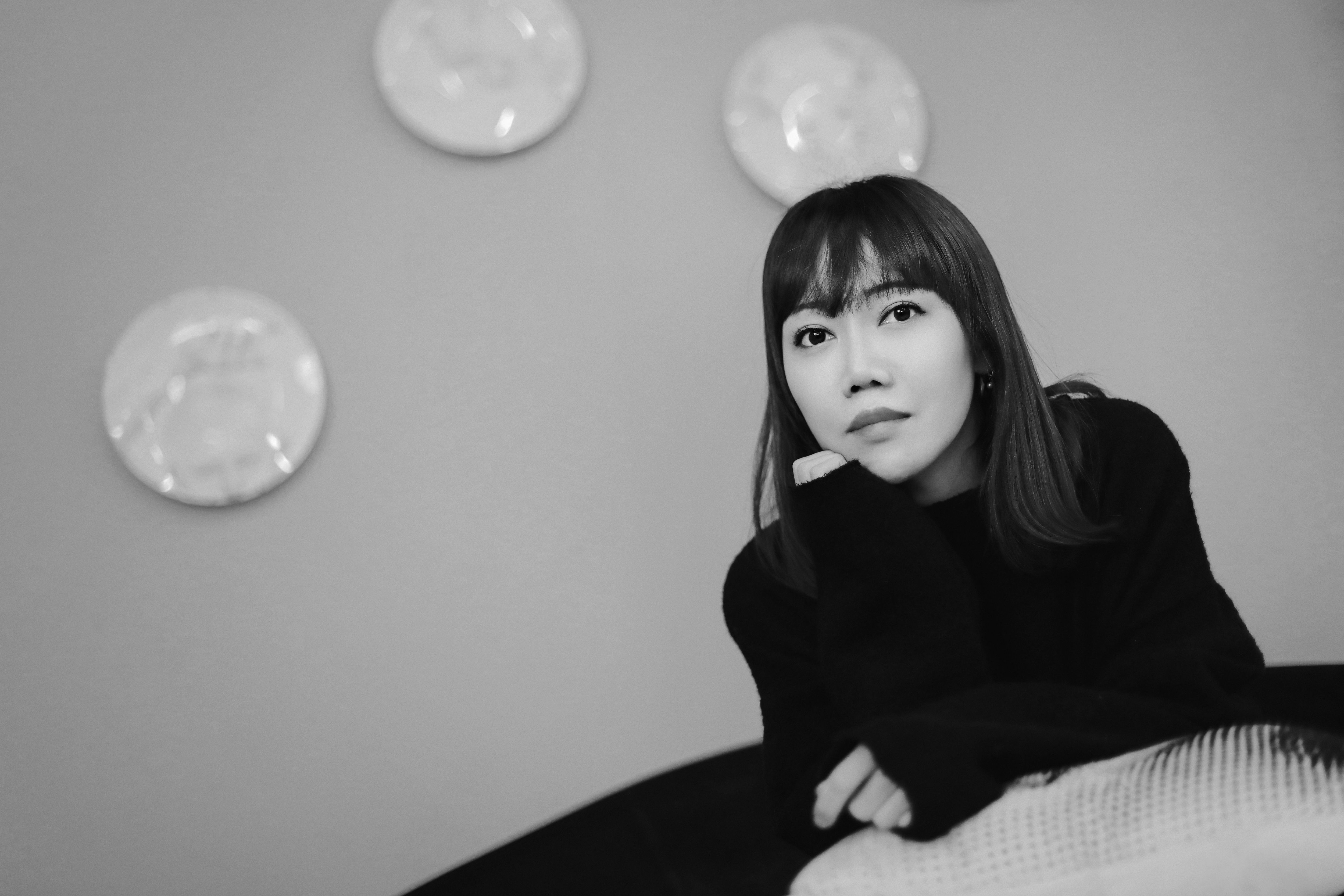 A person in black attire poses thoughtfully against a neutral background.
