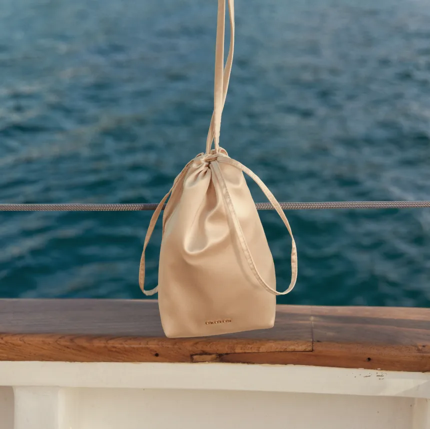 A beige drawstring bag hanging on a boat railing over water.