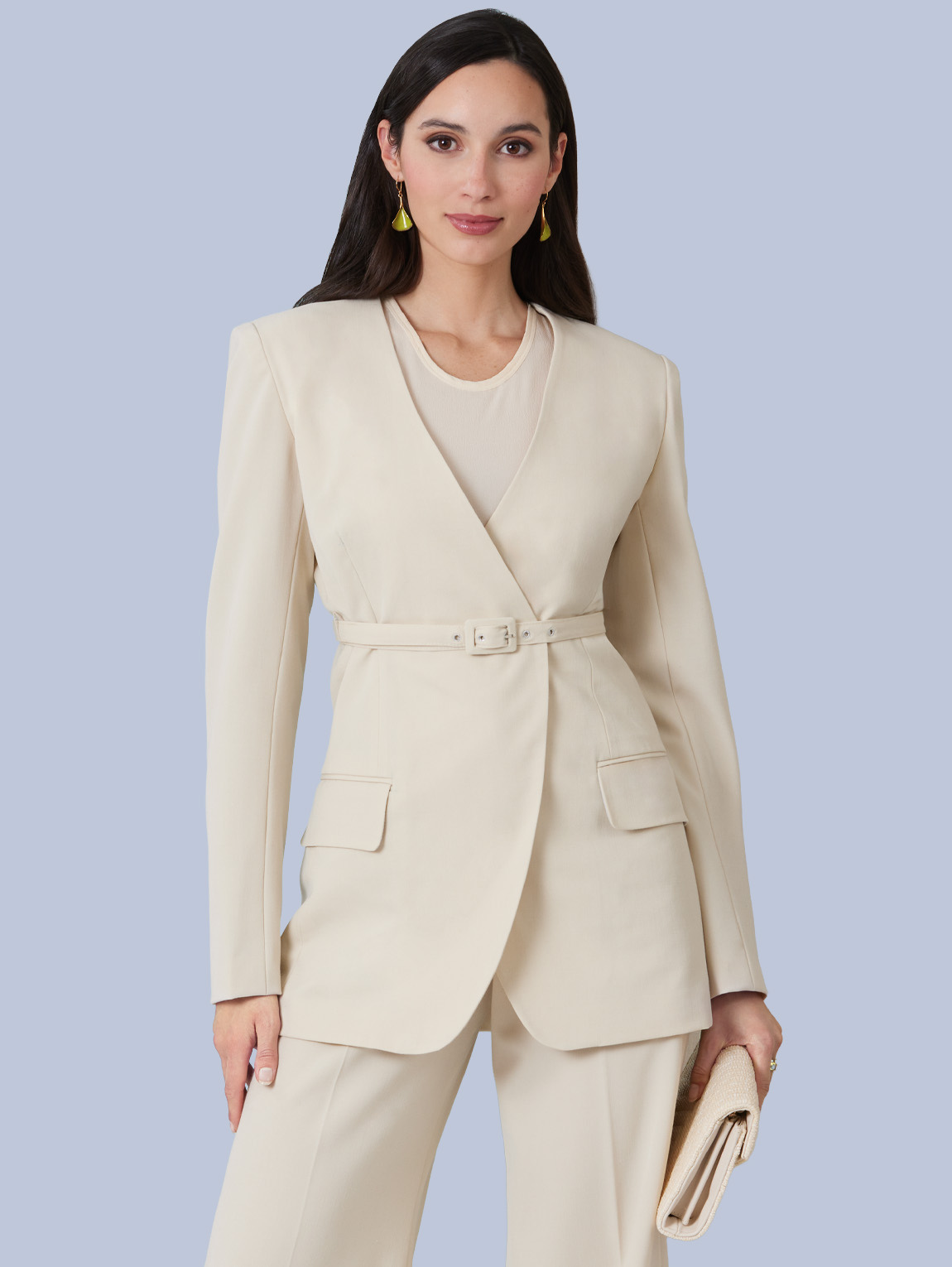 Woman in a cream suit holding a clutch, against a light blue background.