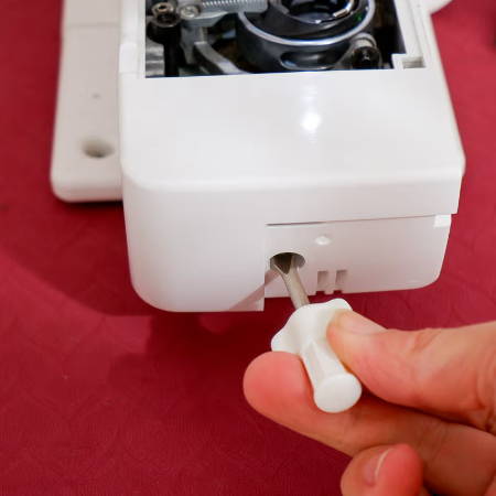 hand with screwdriver to remove the cap of the sewing machine bed