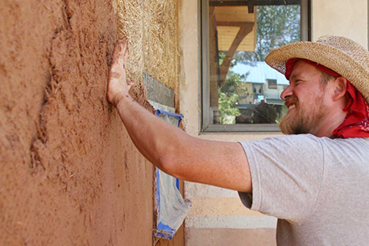 A smiling man plastering the outside of a building
