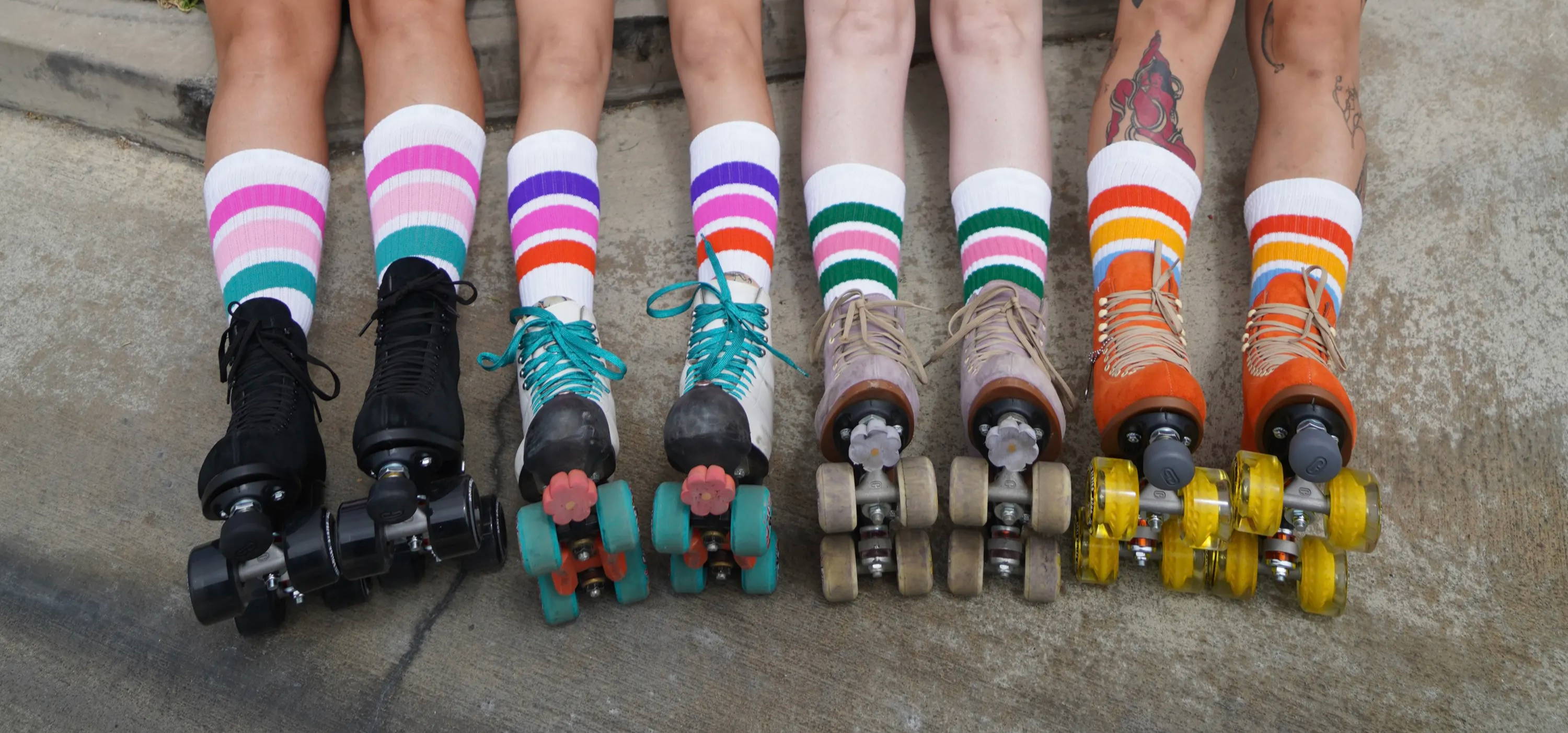 A group of four people from the knees down wearing moxi roller skates of different kinds and colors