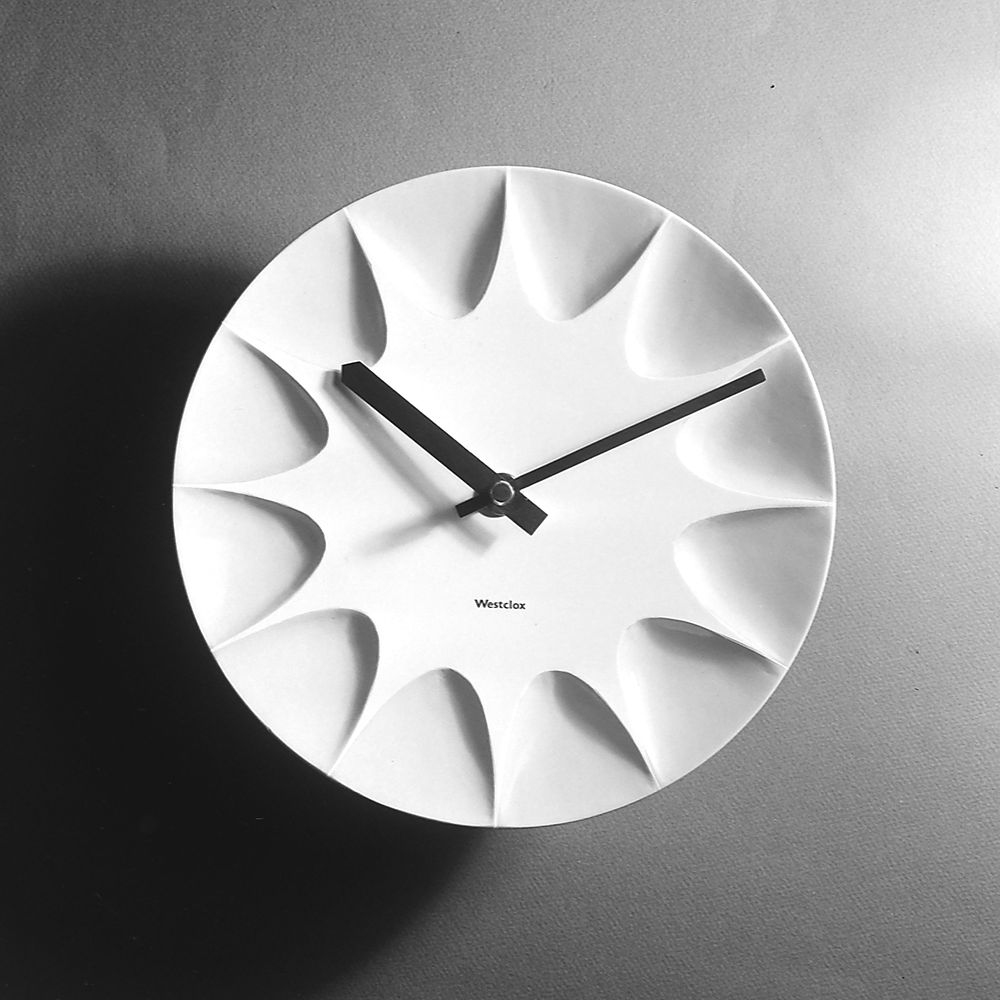 White wall clock with a unique sunburst design and black hands.