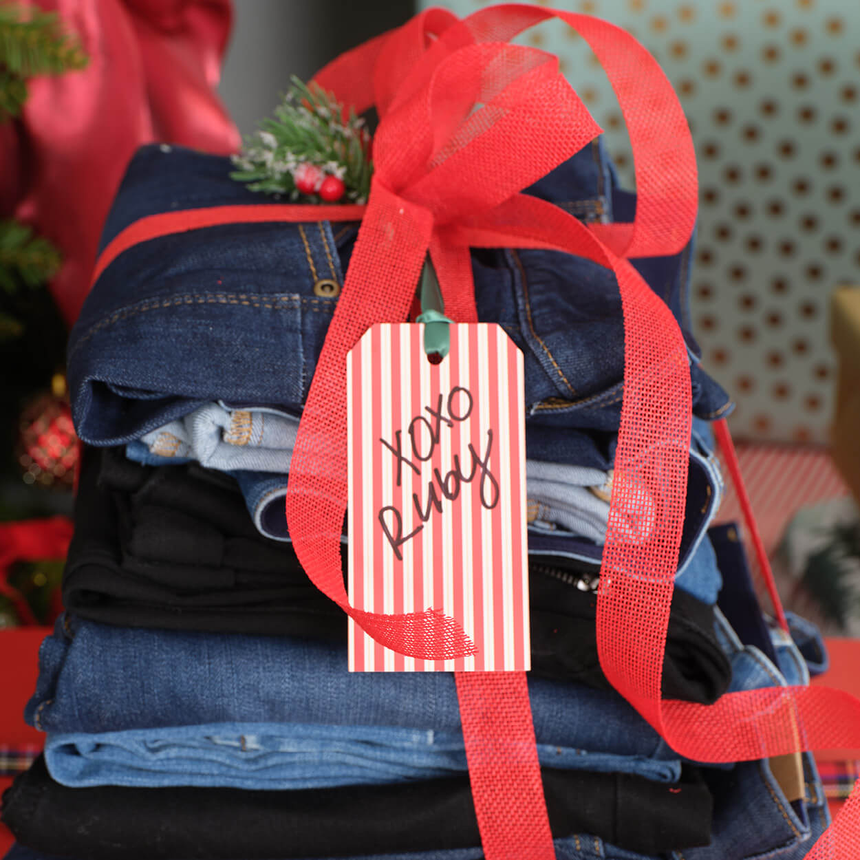 A stack of jeans wrapped with a red ribbon and gift tag.