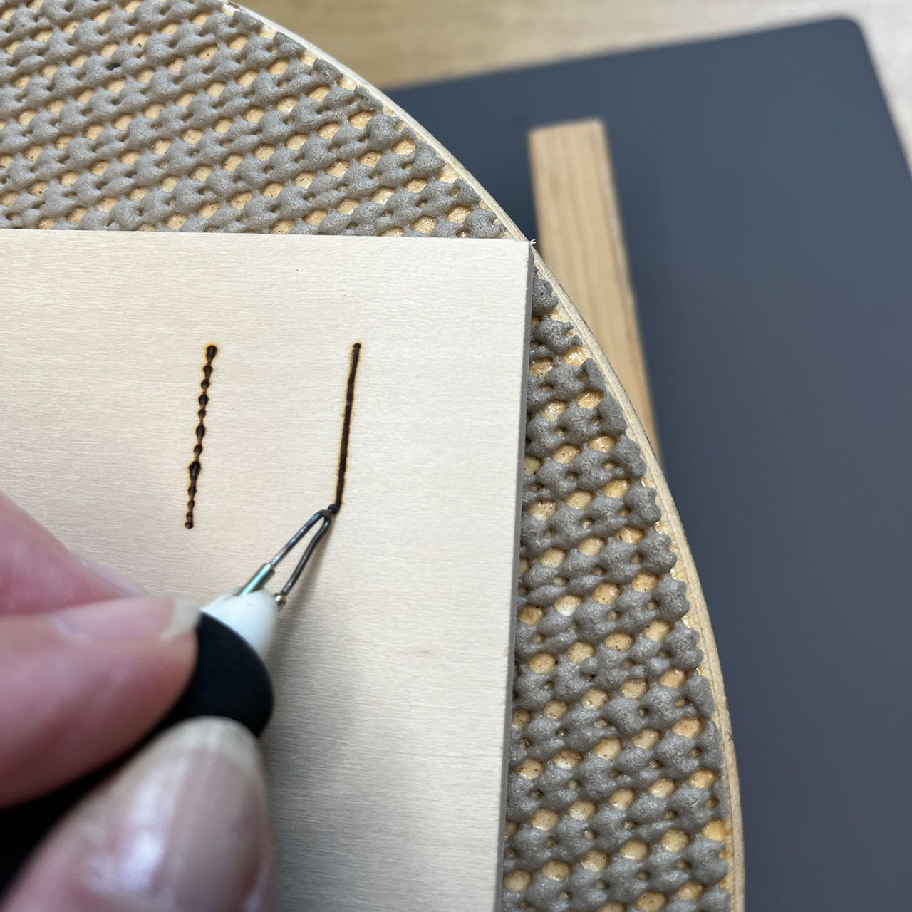 A hand using a pen on a wooden surface with textured background.