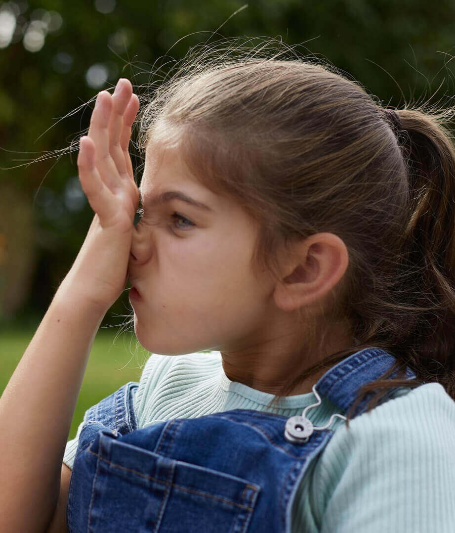Girl with seasonal allergies sat in the garden rubbing her itchy nose upwards with her palm - it’s called the allergic salute