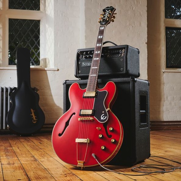 Red electric guitar leaning against a black amplifier in a room.