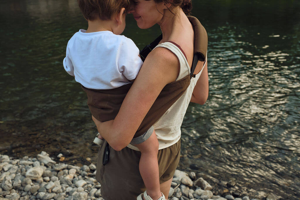 Woman holding a child by a riverbank, both facing each other.