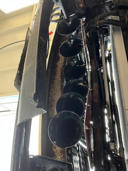 Low-angle view of six black train horns mounted vertically behind front bumper