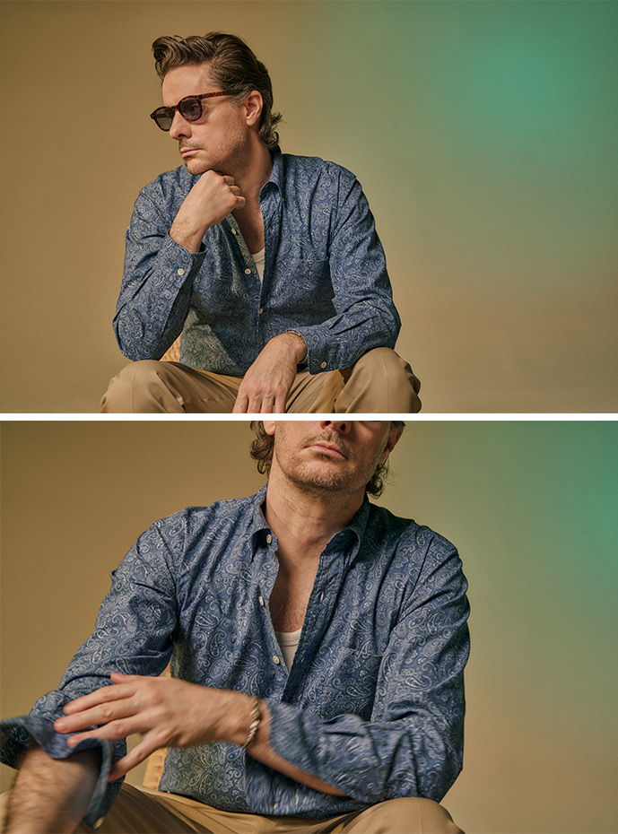 Man in sunglasses wearing a patterned shirt, posing thoughtfully against a gradient background.